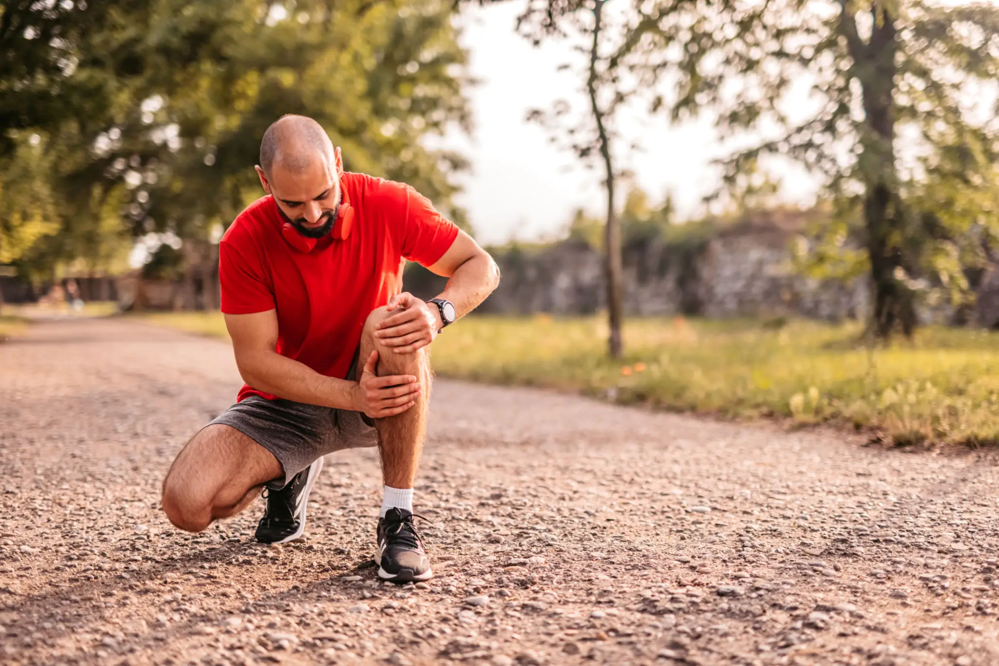 Male runner kneeling and holding his knee in pain outdoors, representing knee injury treatment at Messina Acupuncture PC.