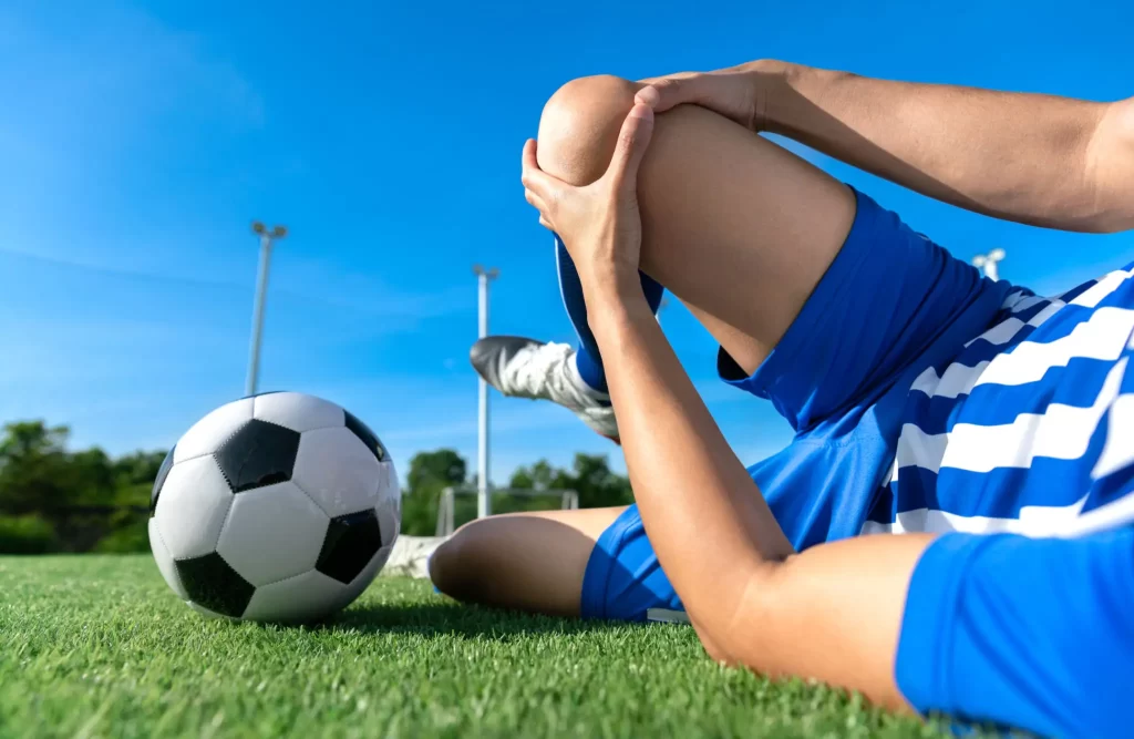 Soccer player holding their knee in pain on the field, representing sports injury and knee pain treatment at Messina Acupuncture PC.
