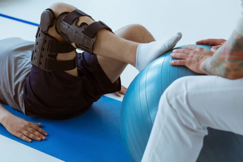 Person performing knee rehabilitation exercises with a brace and stability ball, representing recovery support at Messina Acupuncture PC.