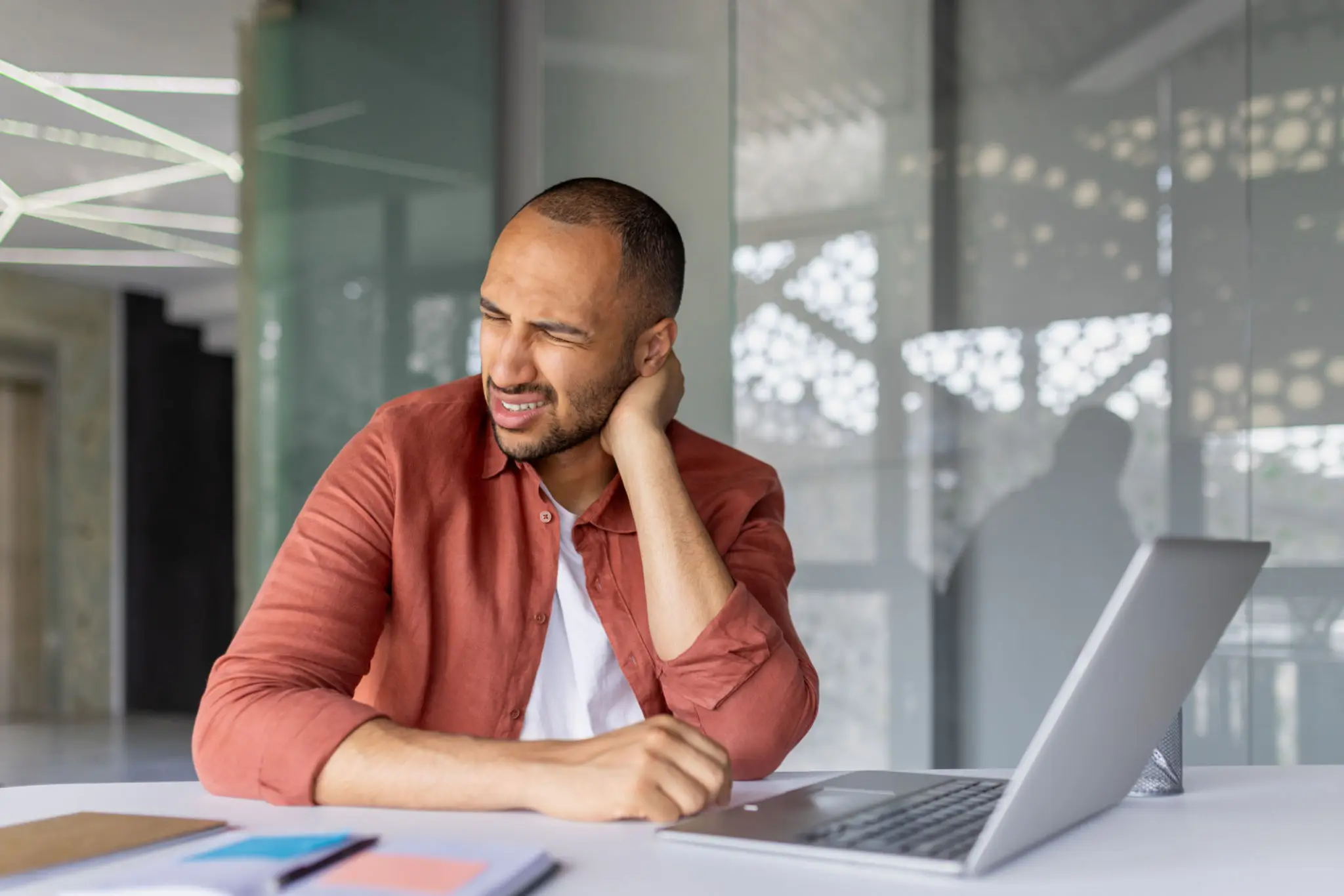 Man at a desk holding his neck in pain, representing posture-related neck strain treated at Messina Acupuncture PC.