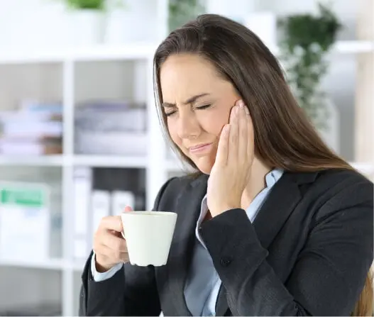 Woman holding jaw in pain from TMJ disorder while drinking coffee, treatable with acupuncture in East Setauket NY